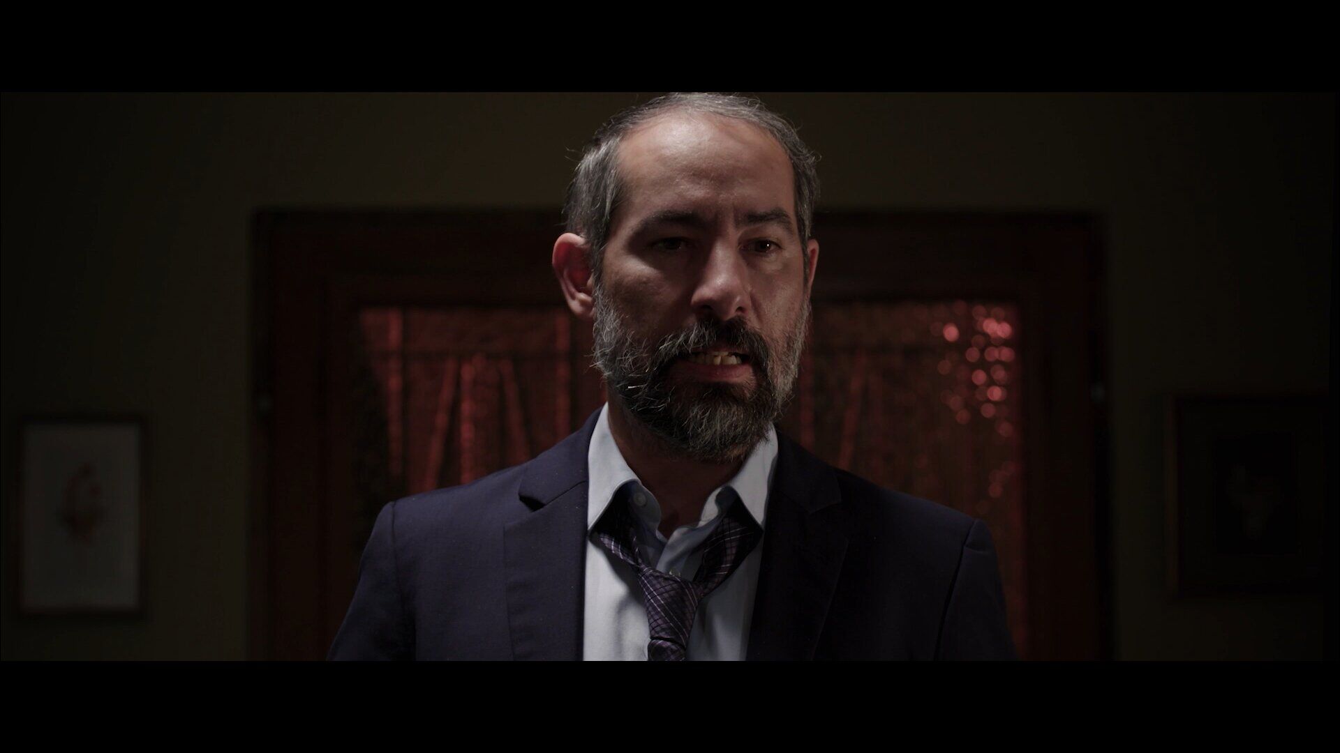 Bearded man framed in a dark motel room interior.