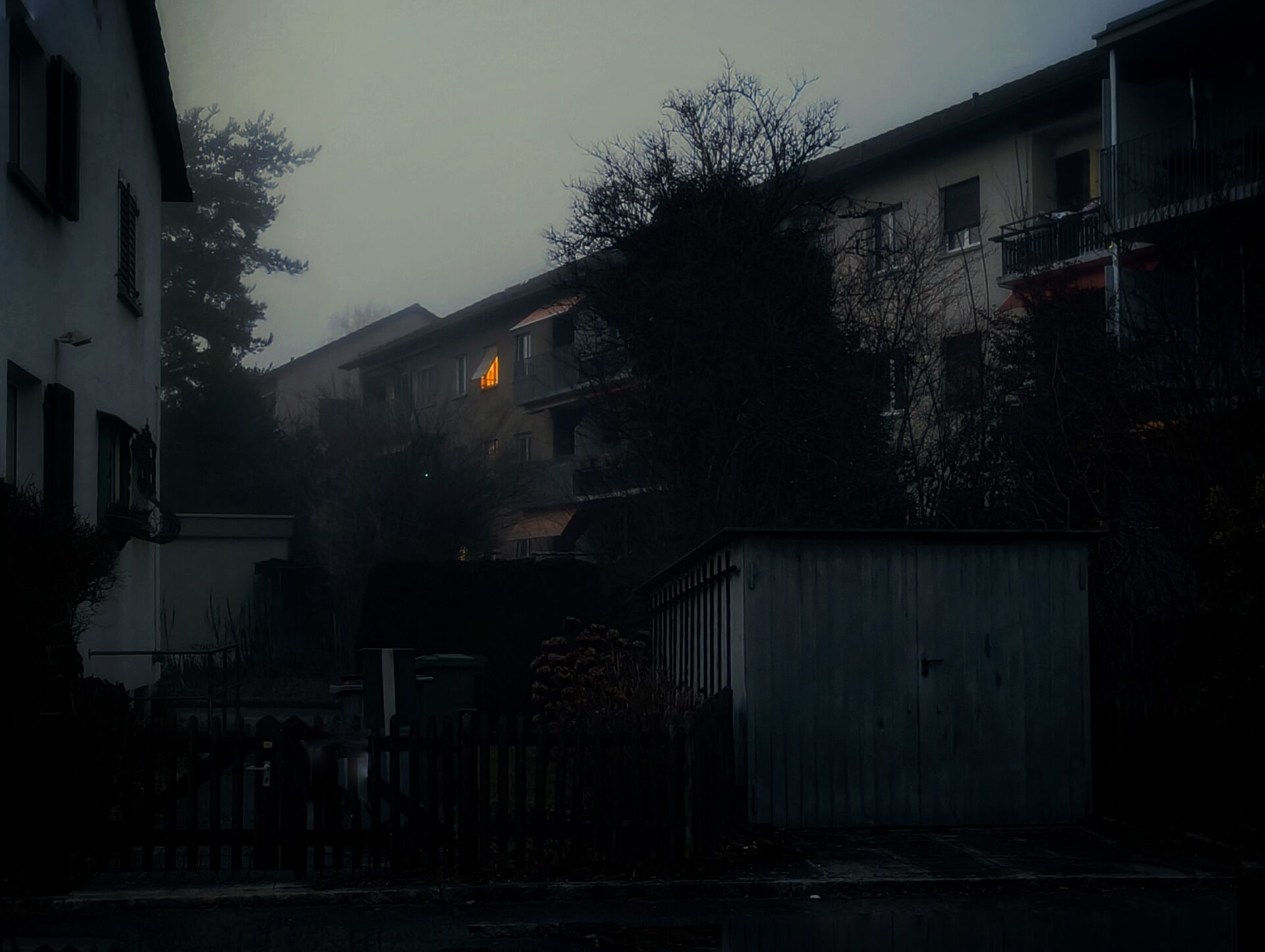 Foggy residential scene with a lit window.